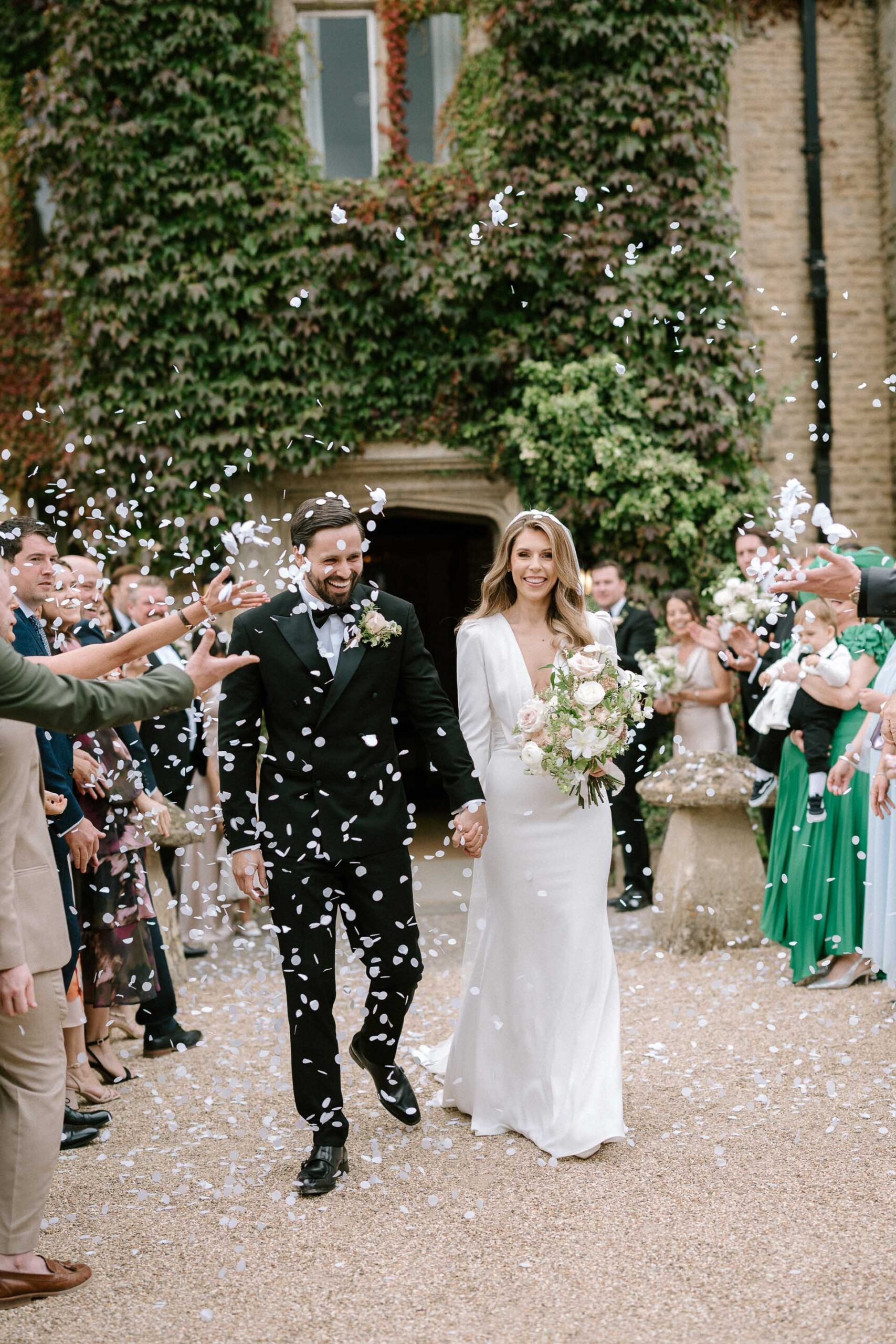 bride and groom walking with guests throwing white paper confetti at the couple