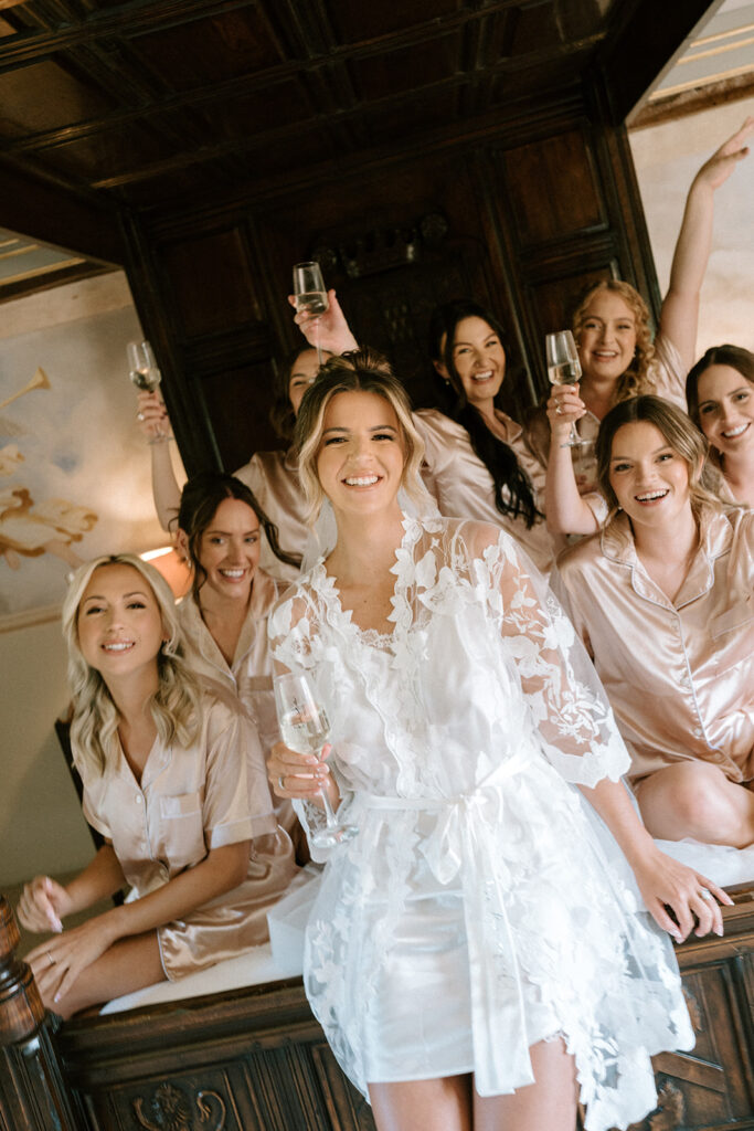 bride and bridal party in pjs on bed cheering with a glass of prosecco