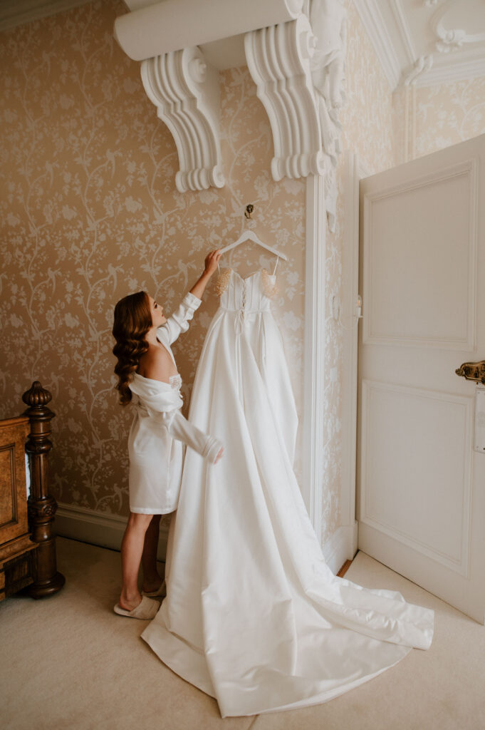 bride holding wedding dress on hanger at harlaxton manor