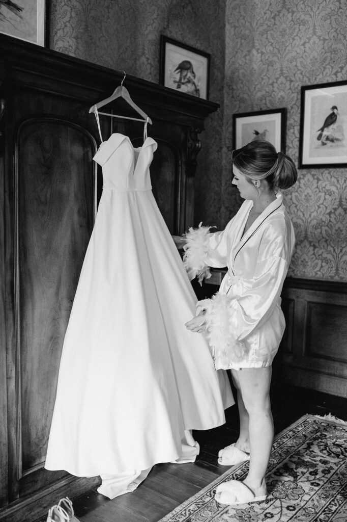 bride holding wedding dress on hanger at glemham hall in Suffolk