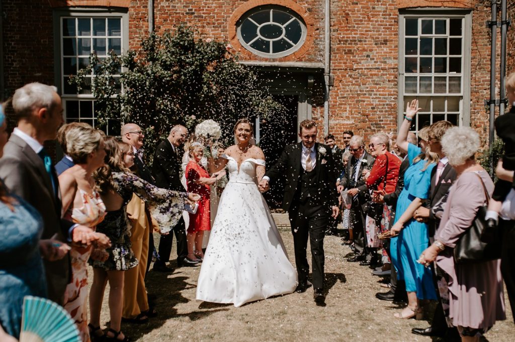 bride and groom walking through confetti line at Glemham Hall