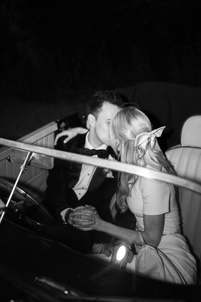 editorial flash image of bride and groom kissing in vintage wedding car