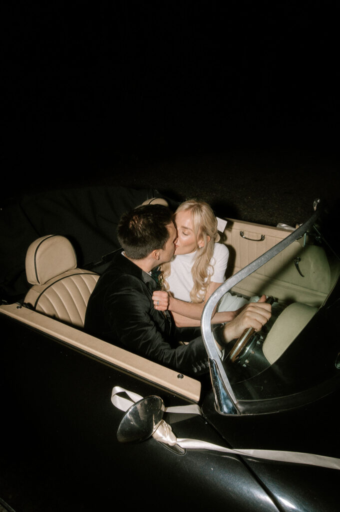 editorial flash image of bride and groom kissing in vintage wedding car