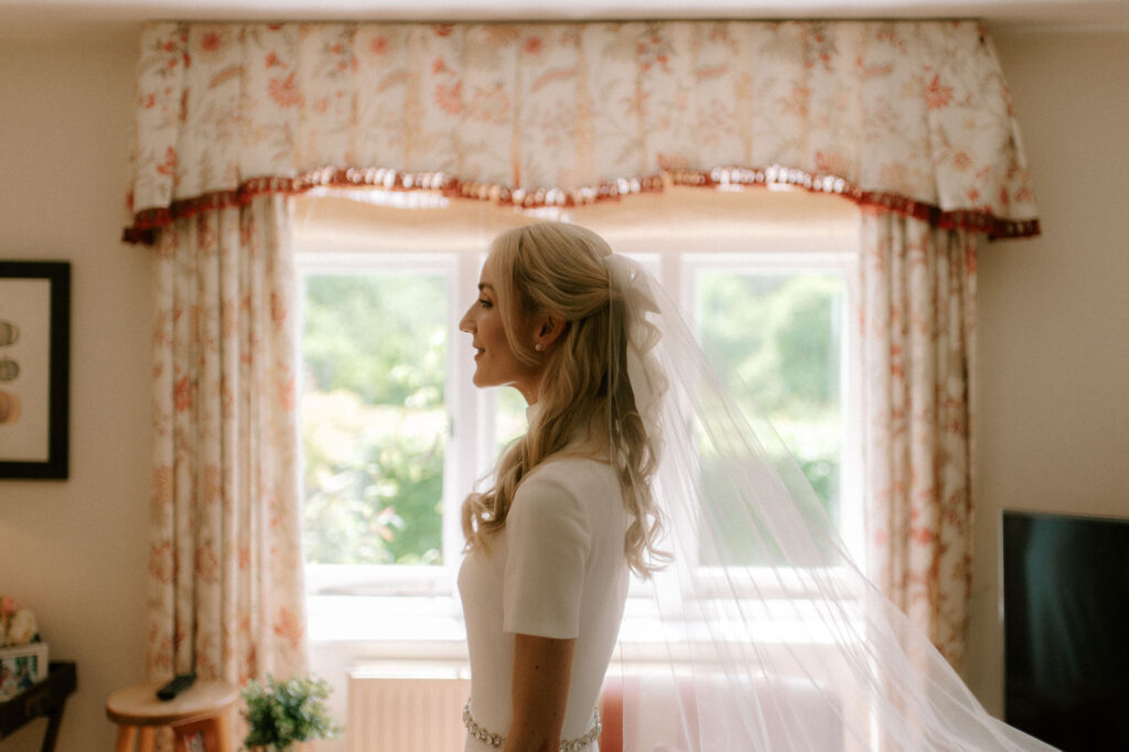 bride in window of family home on wedding morning with veil