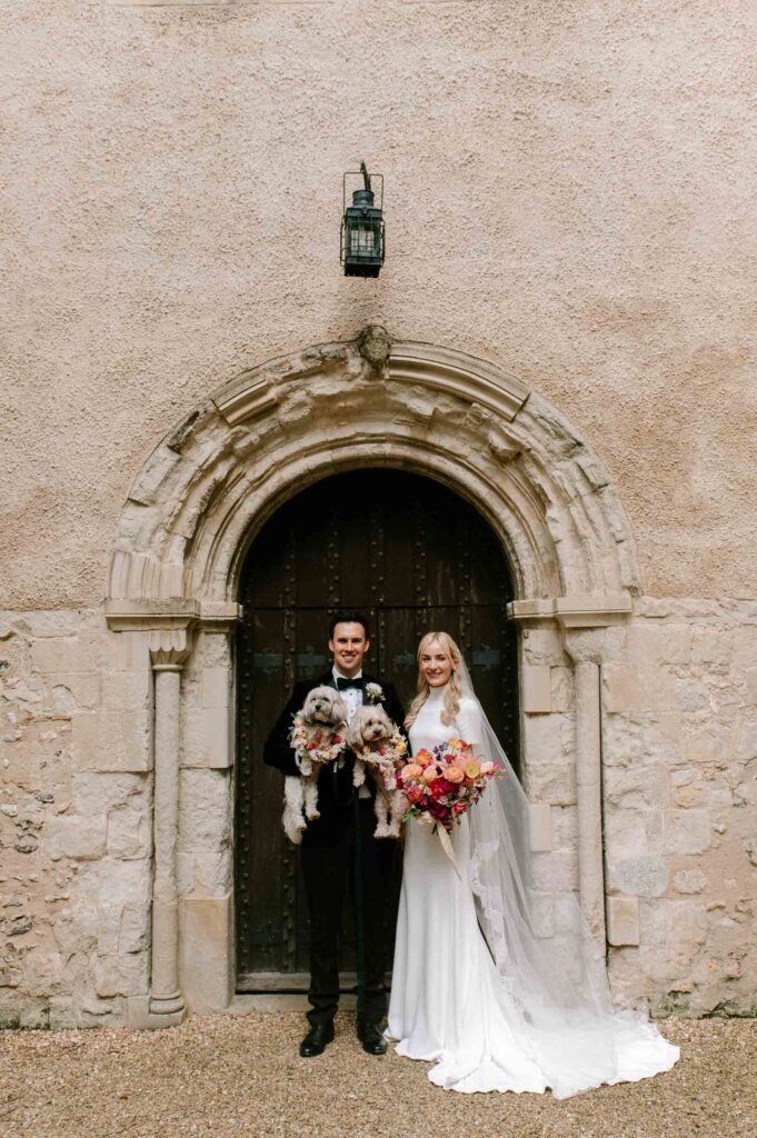 bride and groom smiling outside church in Hampshire after wedding holding 2 dogs