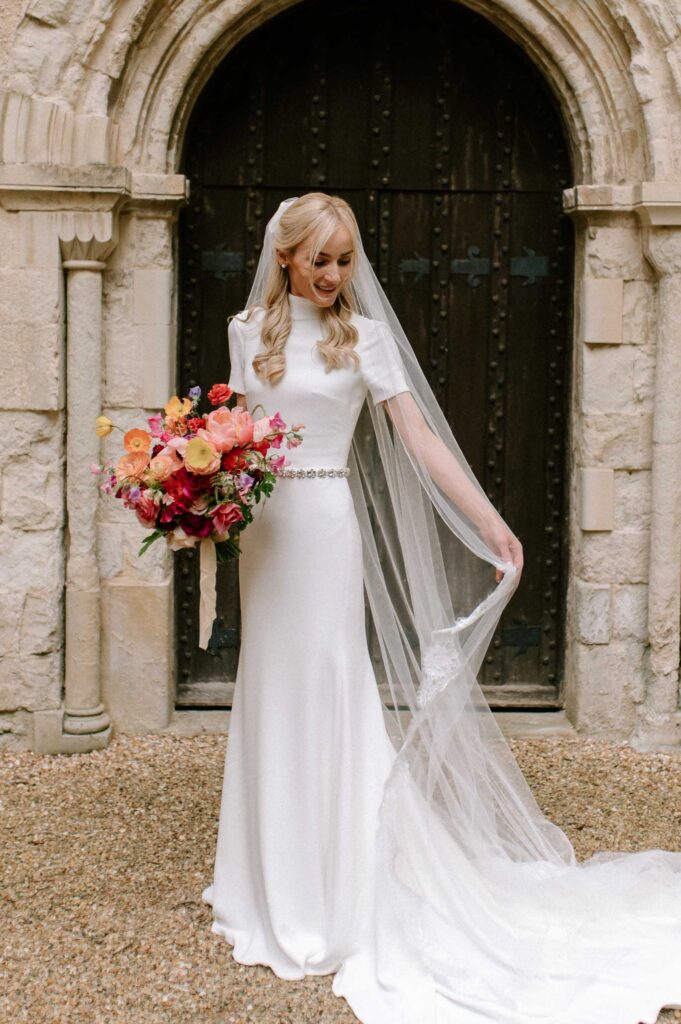 bride outside Hampshire church holding colourful bouquet and adjusting veil