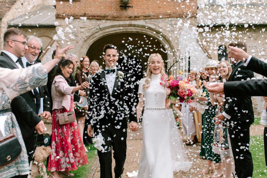 couple walking out of church in Hampshire with guests throwing white confetti