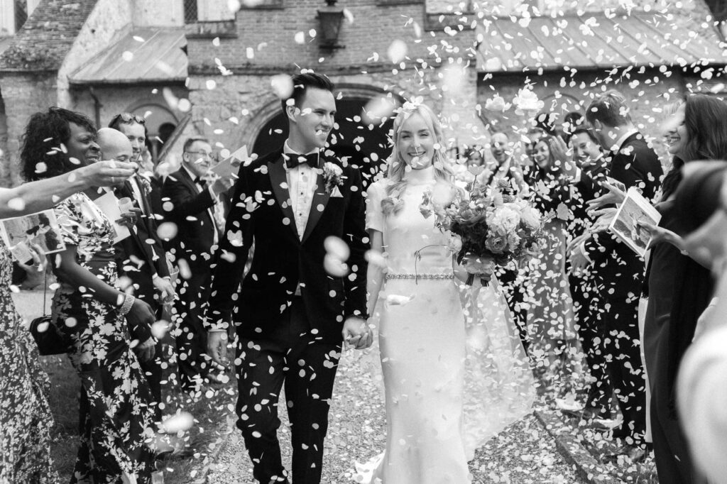 bride and groom walking out of church with guests throwing white paper confetti