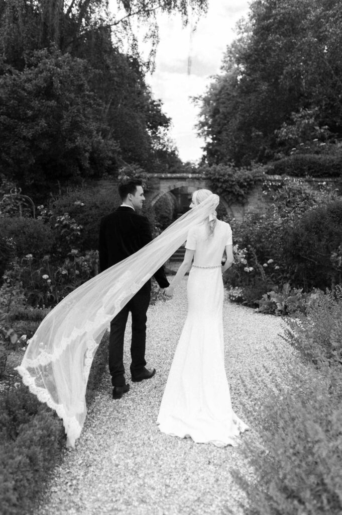 bride and groom walking away in gardens of West Green house gardens wedding venue with veil floating in wind