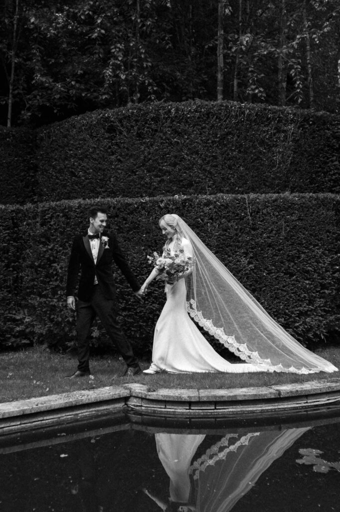 bride and groom walking around lake with veil
