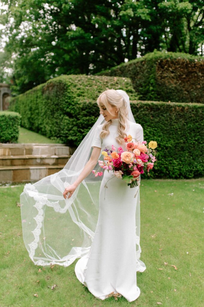 bride adjusting her veil holding colourful bridal bouquet