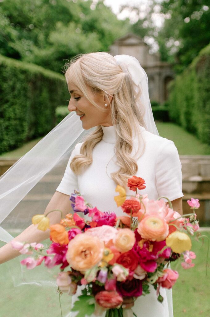 bride adjusting her veil holding colourful bridal bouquet