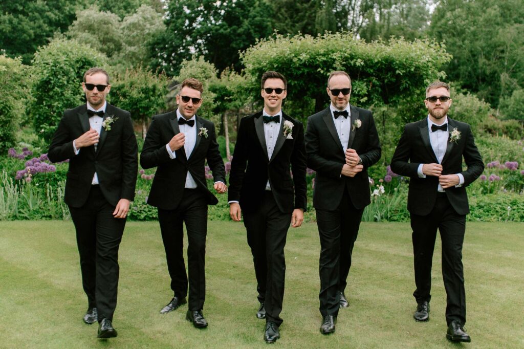 groom walking with groomsmen wearing sunglasses in gardens