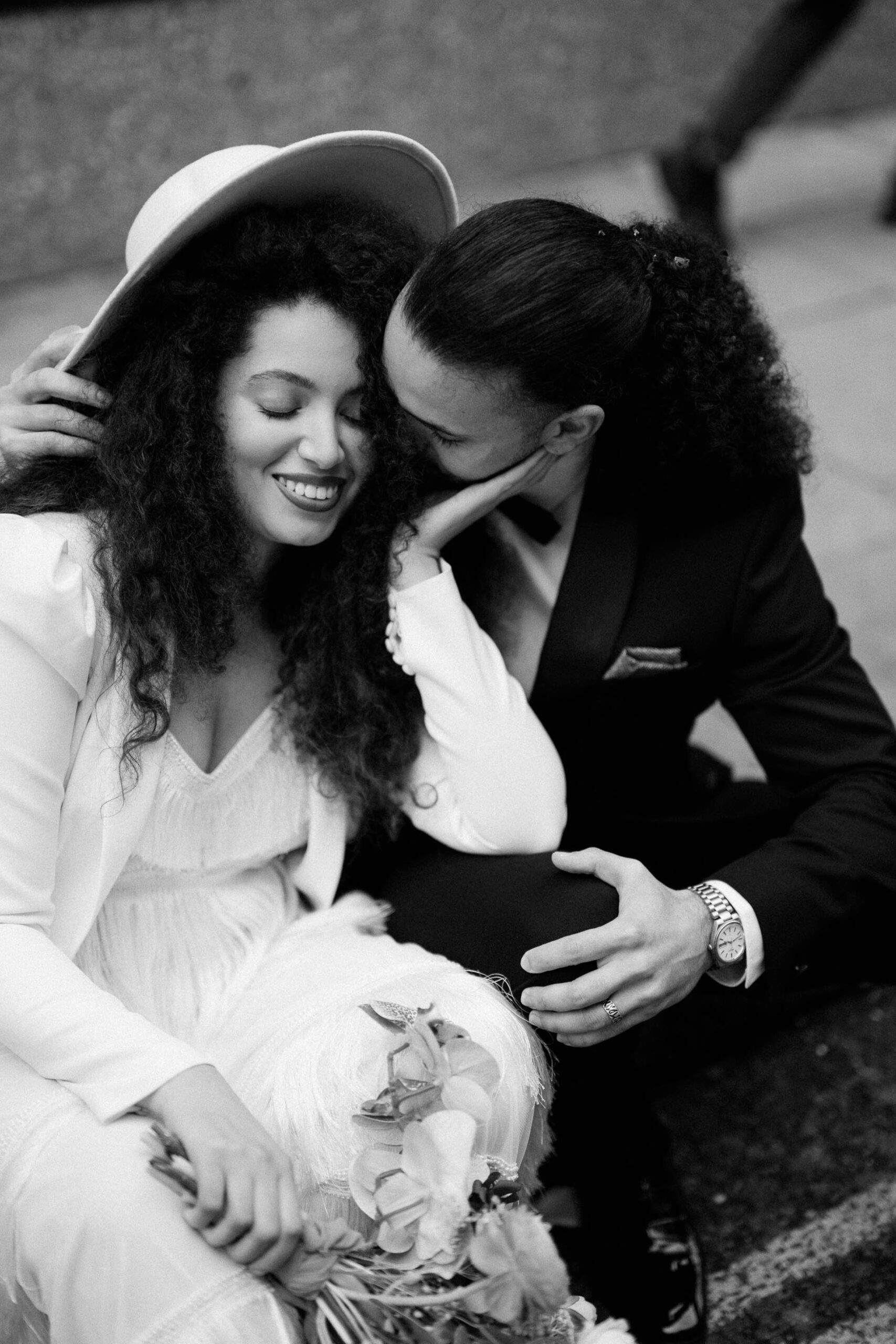 bride and groom sitting on pavement cuddling