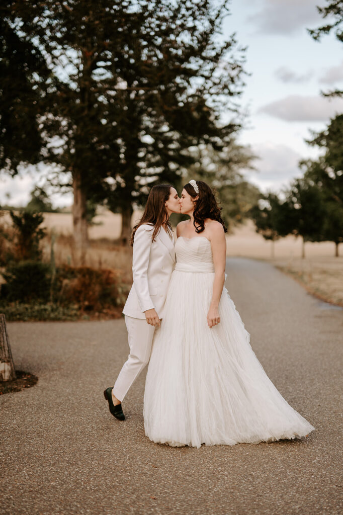 bride wearing off the shoulder wedding dress kissing bride wearing white wedding suit