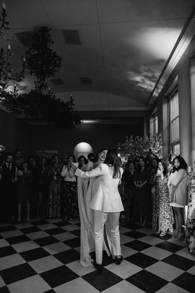two brides having first dance in orangery at wilderness reserve with guests gathered round 