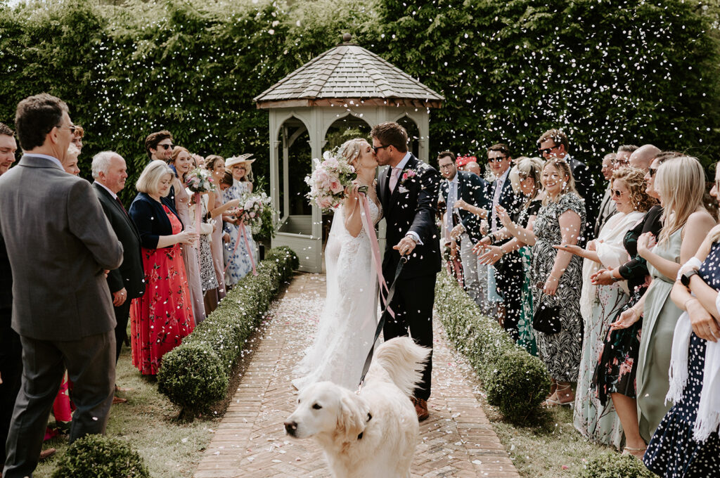 couple walking back down aisle sharing kiss and confetti being thrown by guests at retreat east