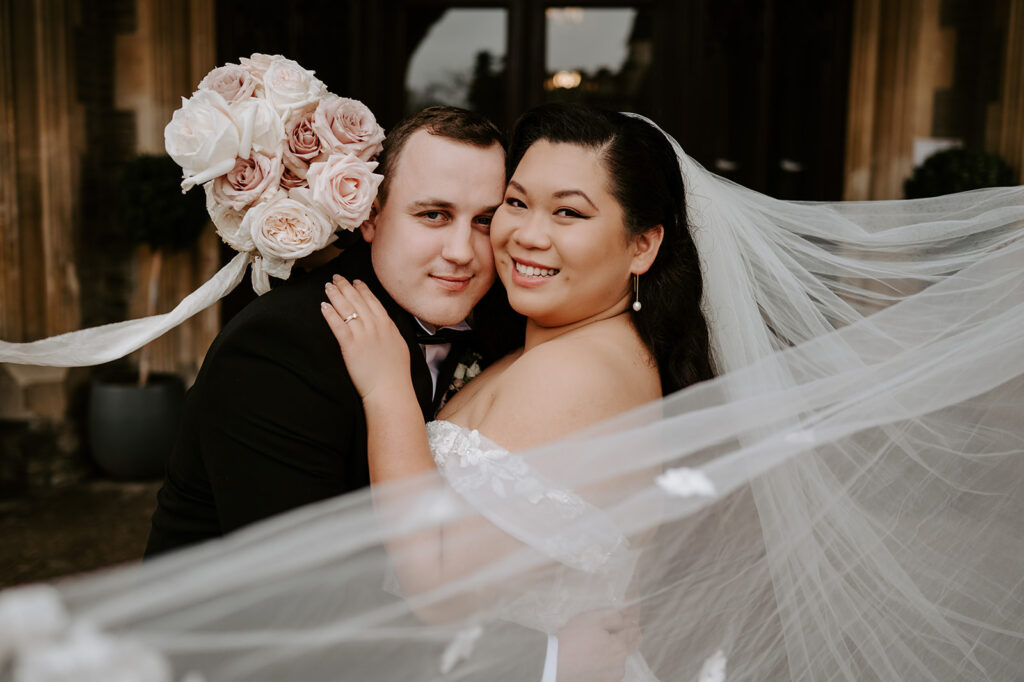 bride and groom with veil floating in wind holding blush pink rose bouquet