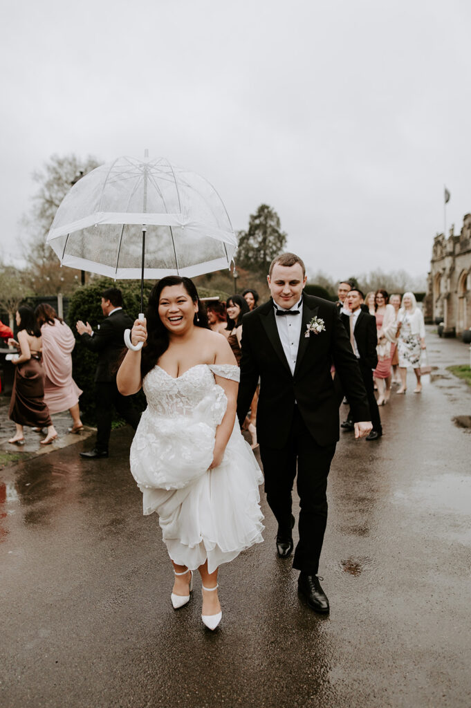 bride and groom with clear umbrella walking in the rain at tortworth court