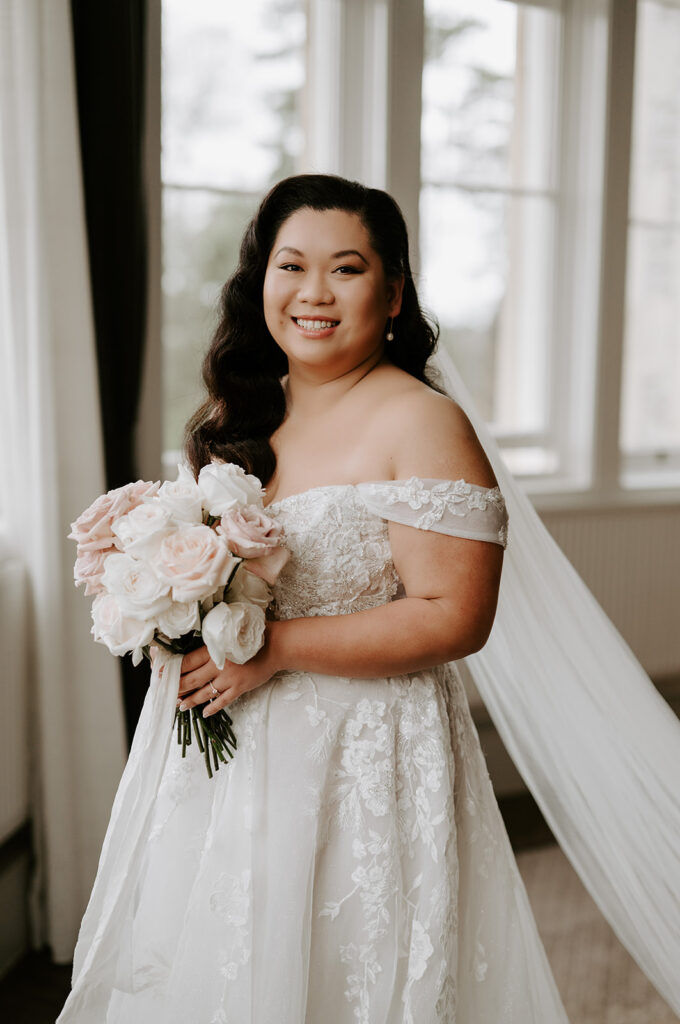 bride smiling holding blush pink rose bouquet wearing dress at tortworth court