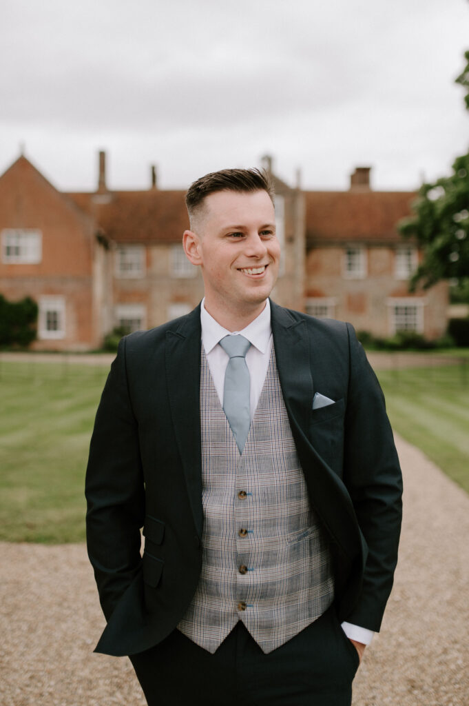 Groom standing outside Bruisyard Hall in his suit before the ceremony