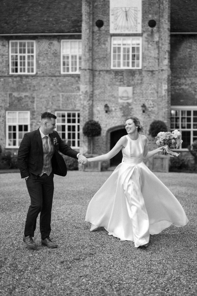 Bride and groom holding hands and spinning together outside Bruisyard Hall