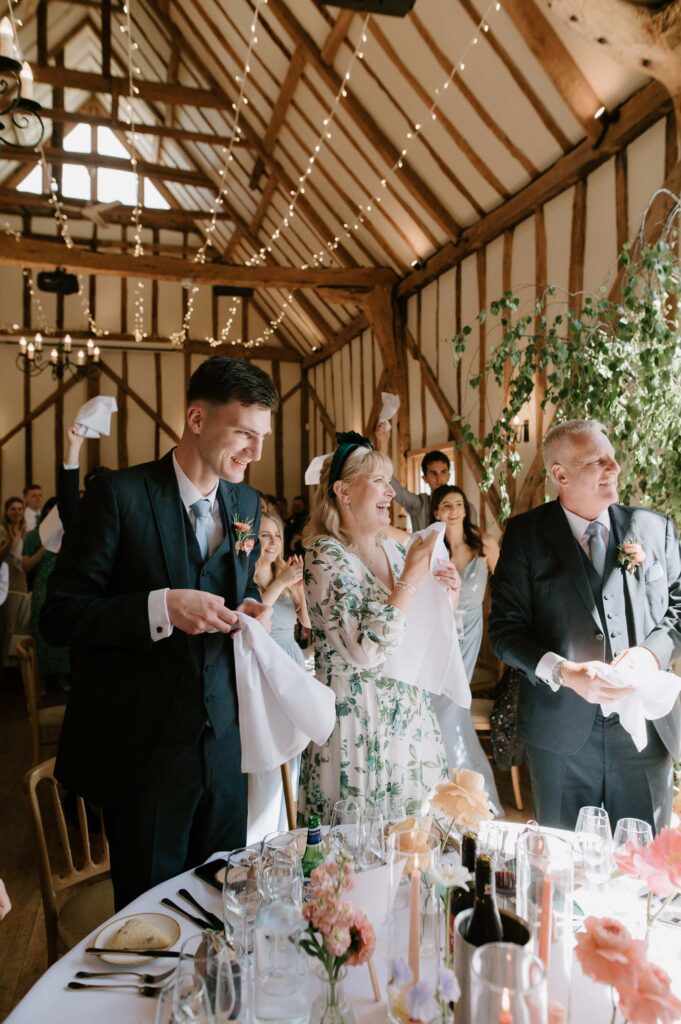 guests cheering at top table as bride and groom enter reception room at bruisyard hall