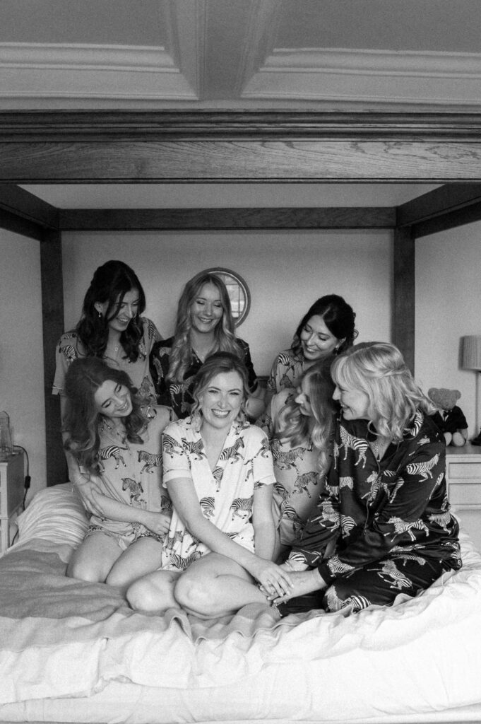 Bridesmaids sitting together on the bed in their pjs during bridal prep at Bruisyard Hall