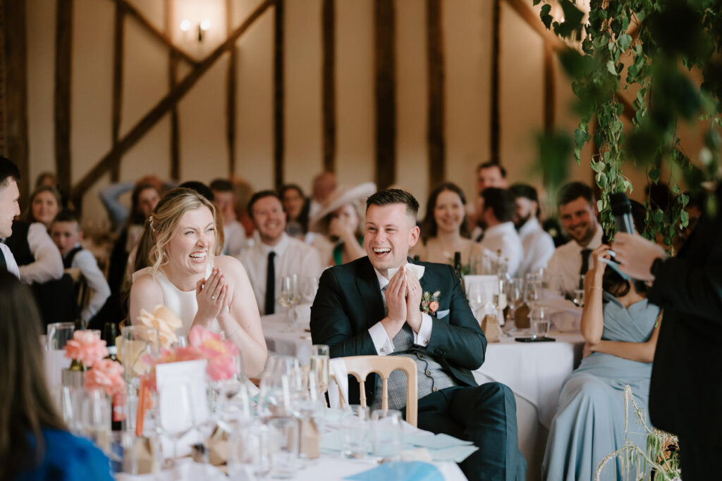 Bride and groom smiling and holding microphones during their wedding speeches