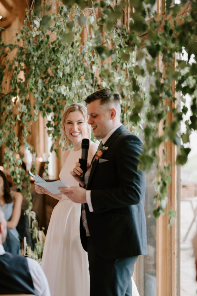 Bride and groom standing together while holding microphones during speeches at Bruisyard Hall