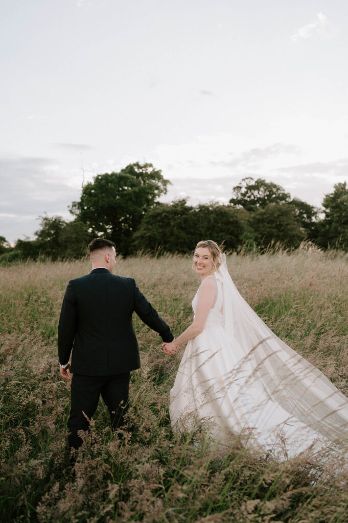 bride and groom walking off in field at bruisyard hall