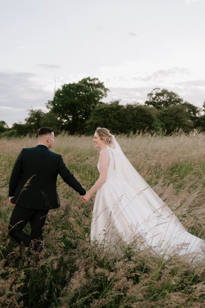 bride and groom walking off and talking in field at bruisyard hall