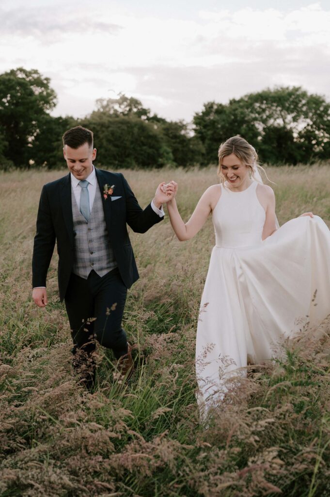 bride and groom walking towards camera in field at bruisyard hall