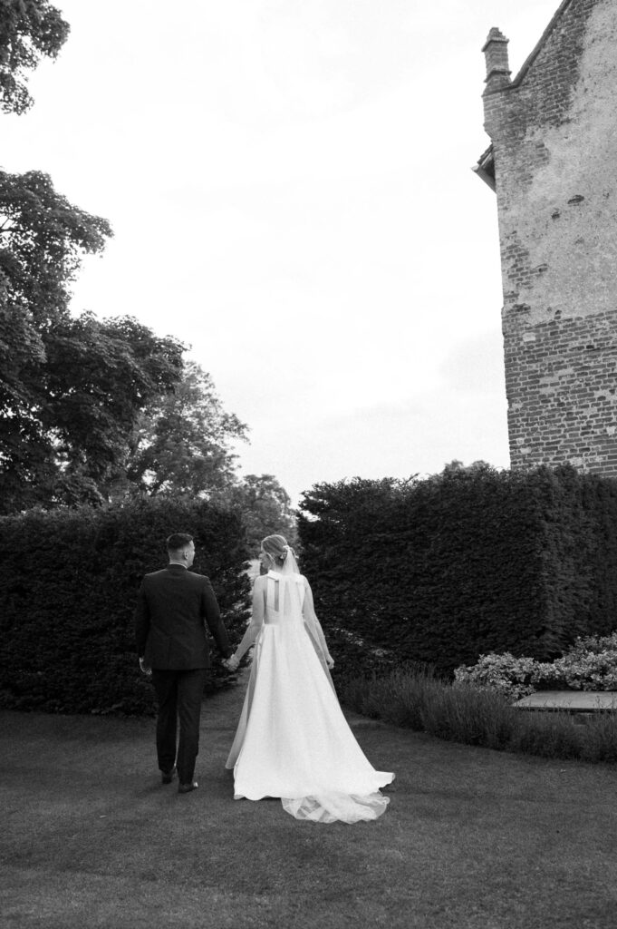 Bride and groom walking away together through the gardens at Bruisyard Hall