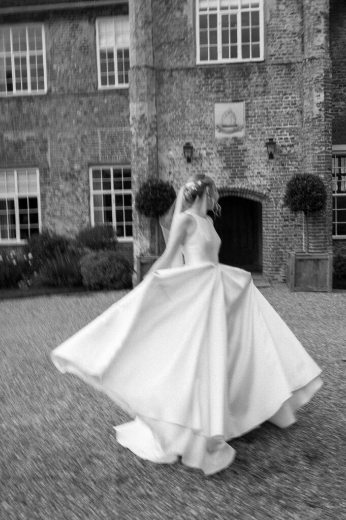 Bride spinning her dress with the groom watching at Bruisyard Hall