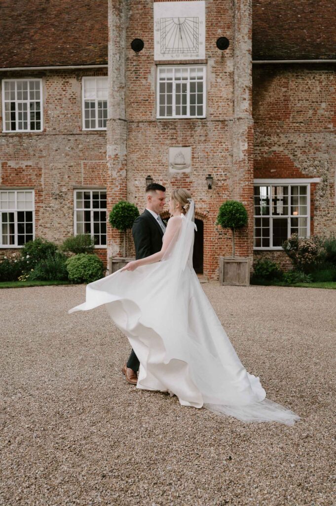 Bride and groom standing together with the bride’s dress flowing at Bruisyard Hall
