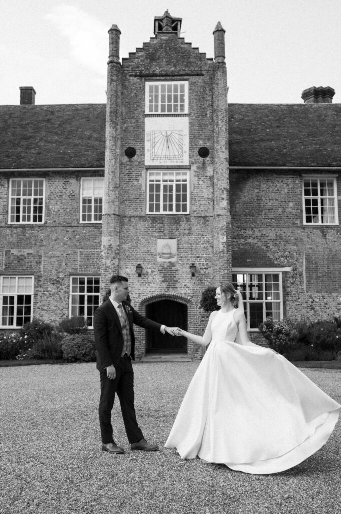 Bride and groom standing apart with the bride holding her dress at Bruisyard Hall