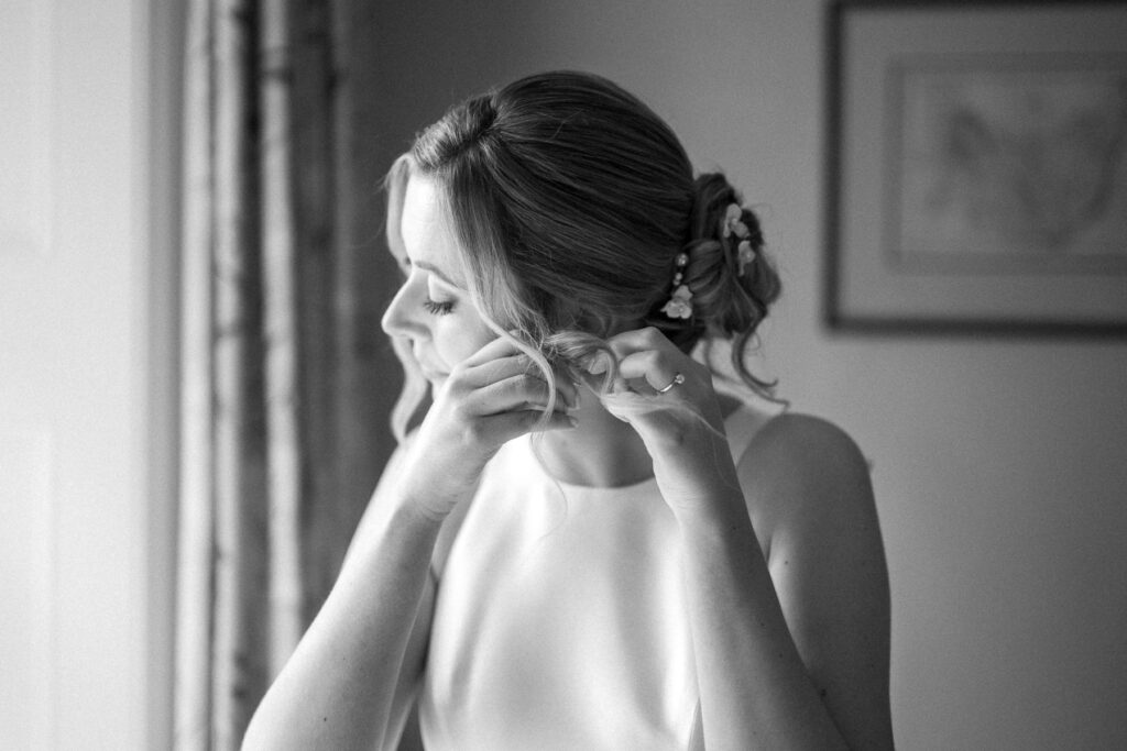 Black and white portrait of bride Heidi putting in her earrings during bridal prep