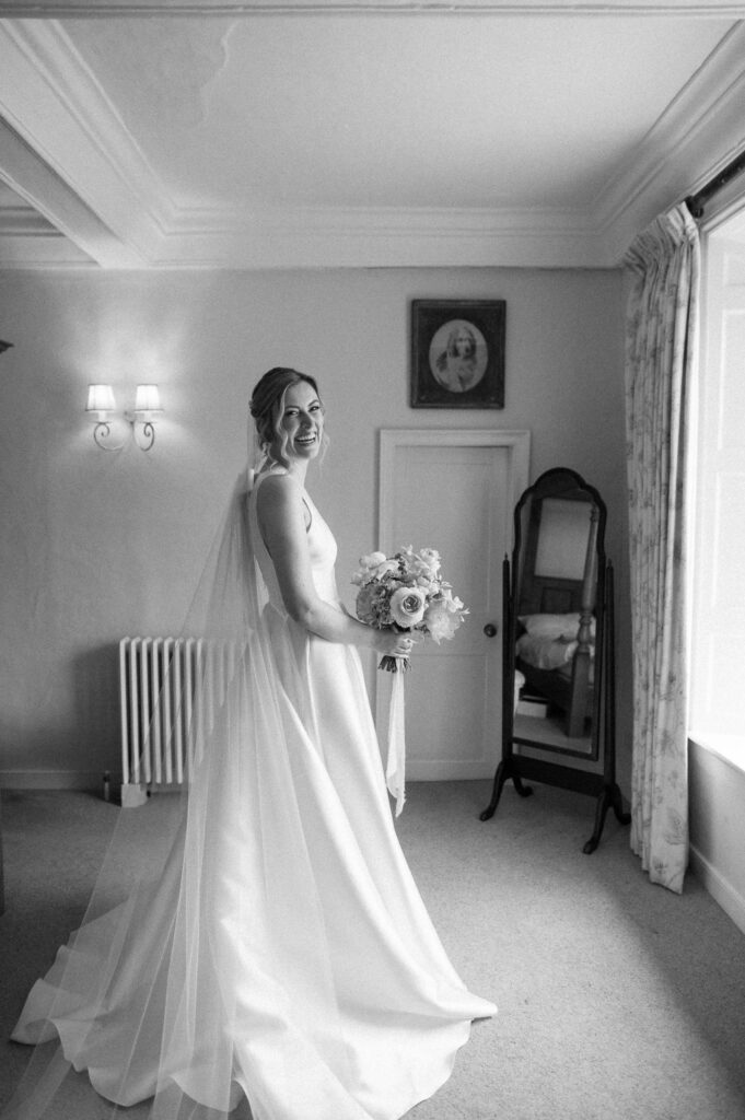 Bride Heidi smiling and holding her bouquet by the window just before walking to the ceremony at Bruisyard Hall