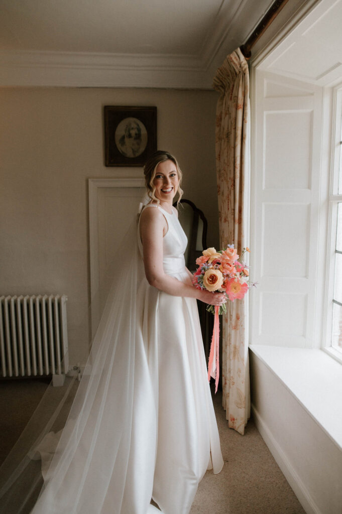 Bride Heidi smiling and holding her bouquet just before walking to the ceremony at Bruisyard Hall