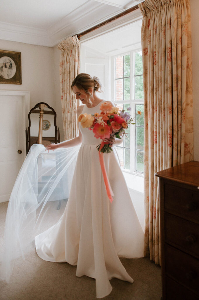 Bride Heidi adjusting her wedding dress and veil during prep at Bruisyard Hall