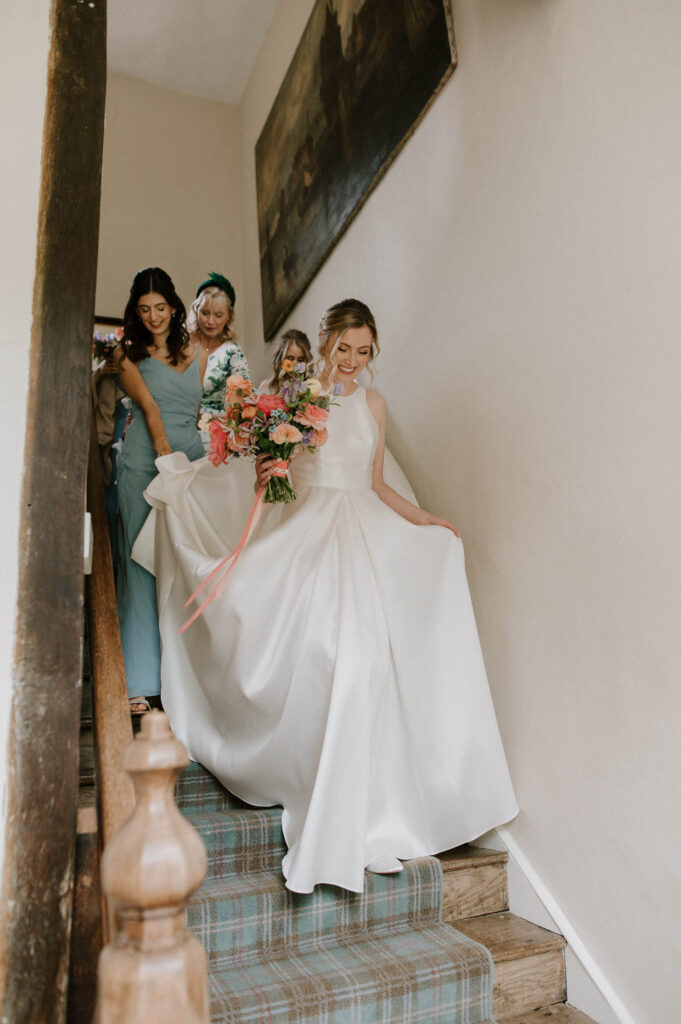 Bride Heidi walking down the stairs with her bridesmaids on the way to the ceremony at Bruisyard Hall