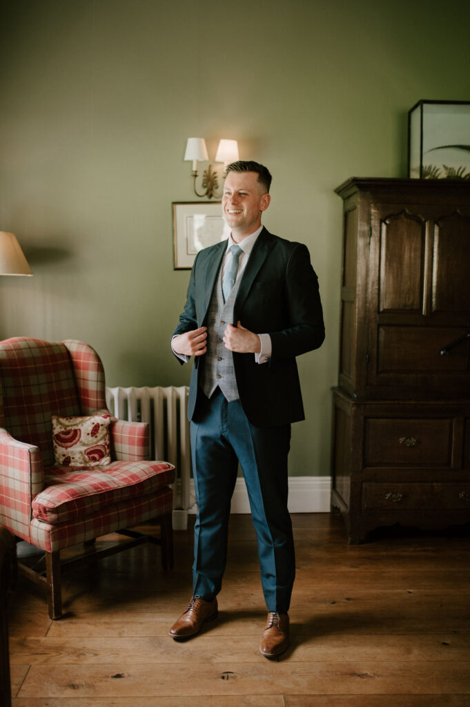 Groom adjusting his jacket in the green room during prep at Bruisyard Hall