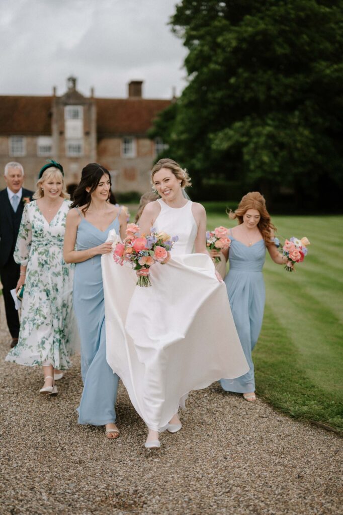 Bride Heidi and her bridesmaids walking along the path towards the ceremony at Bruisyard Hall in summer