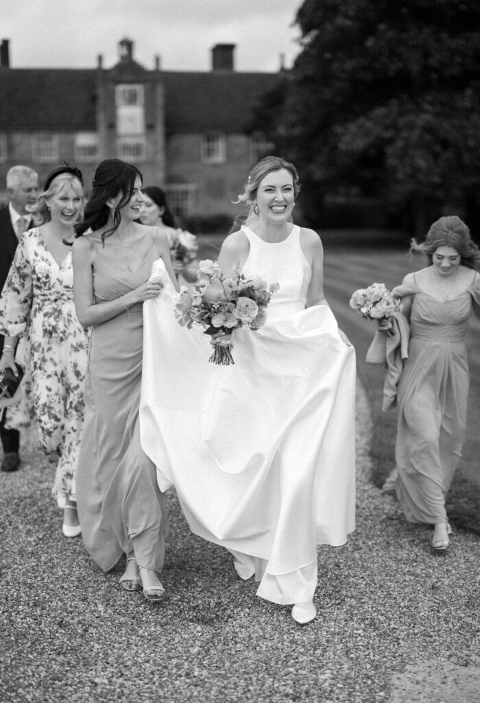 Black and white photo of bride and bridal party walking together to the ceremony at Bruisyard Hall