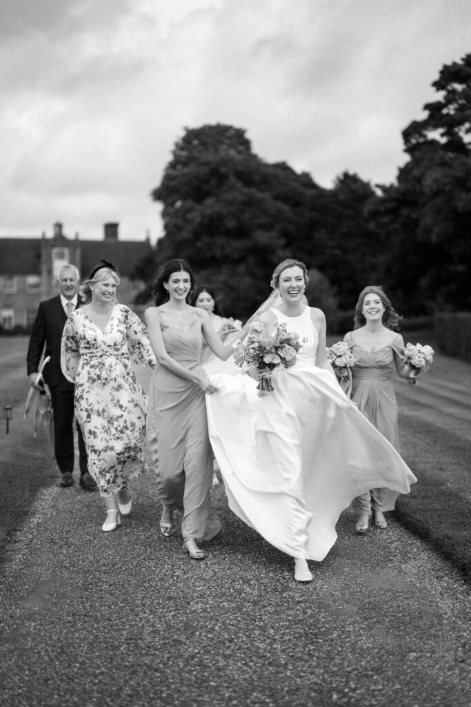 Bride Heidi walking to the ceremony with her bridesmaids outside Bruisyard Hall on a summer wedding day