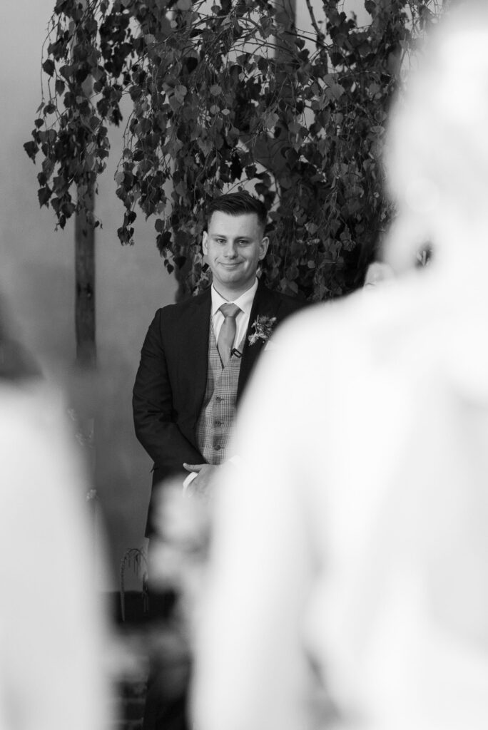 Groom smiling as he sees bride during the ceremony at Bruisyard Hall