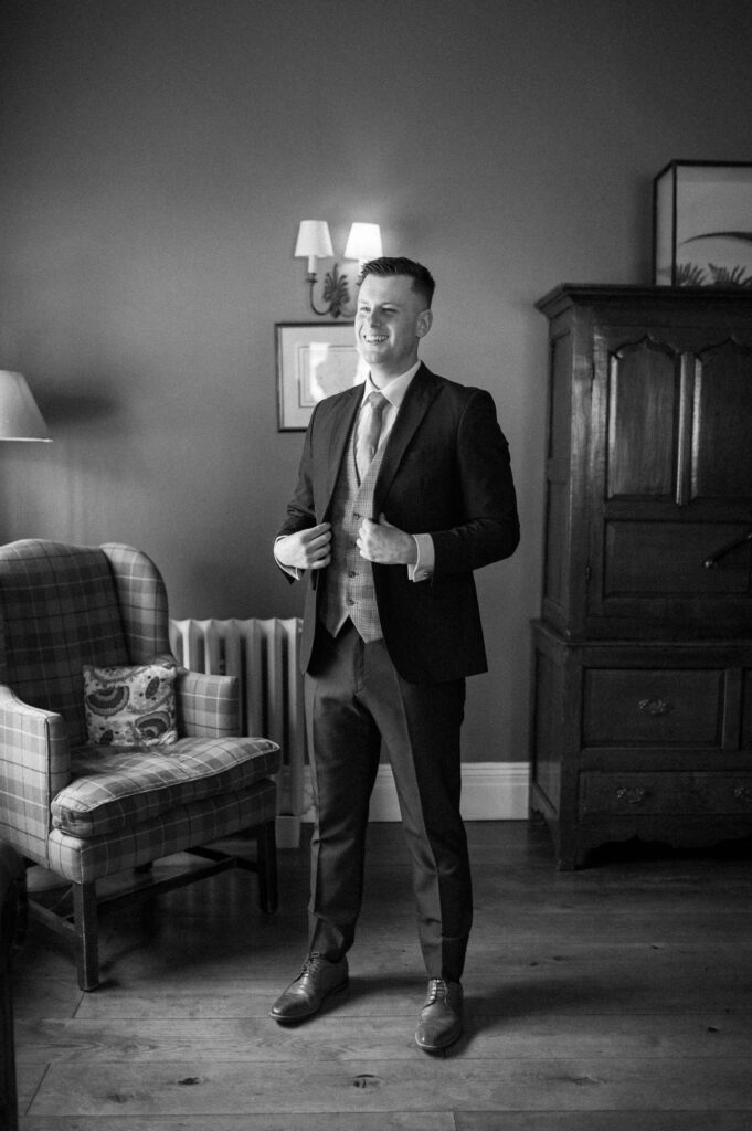 Black and white photo of groom Charley adjusting his jacket during prep at Bruisyard Hall