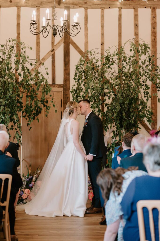 Bride and groom sharing a first kiss during their ceremony at Bruisyard Hall