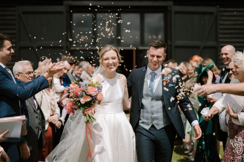 Bride and Groom walking hand in hand through confetti after their ceremony at Bruisyard Hall
